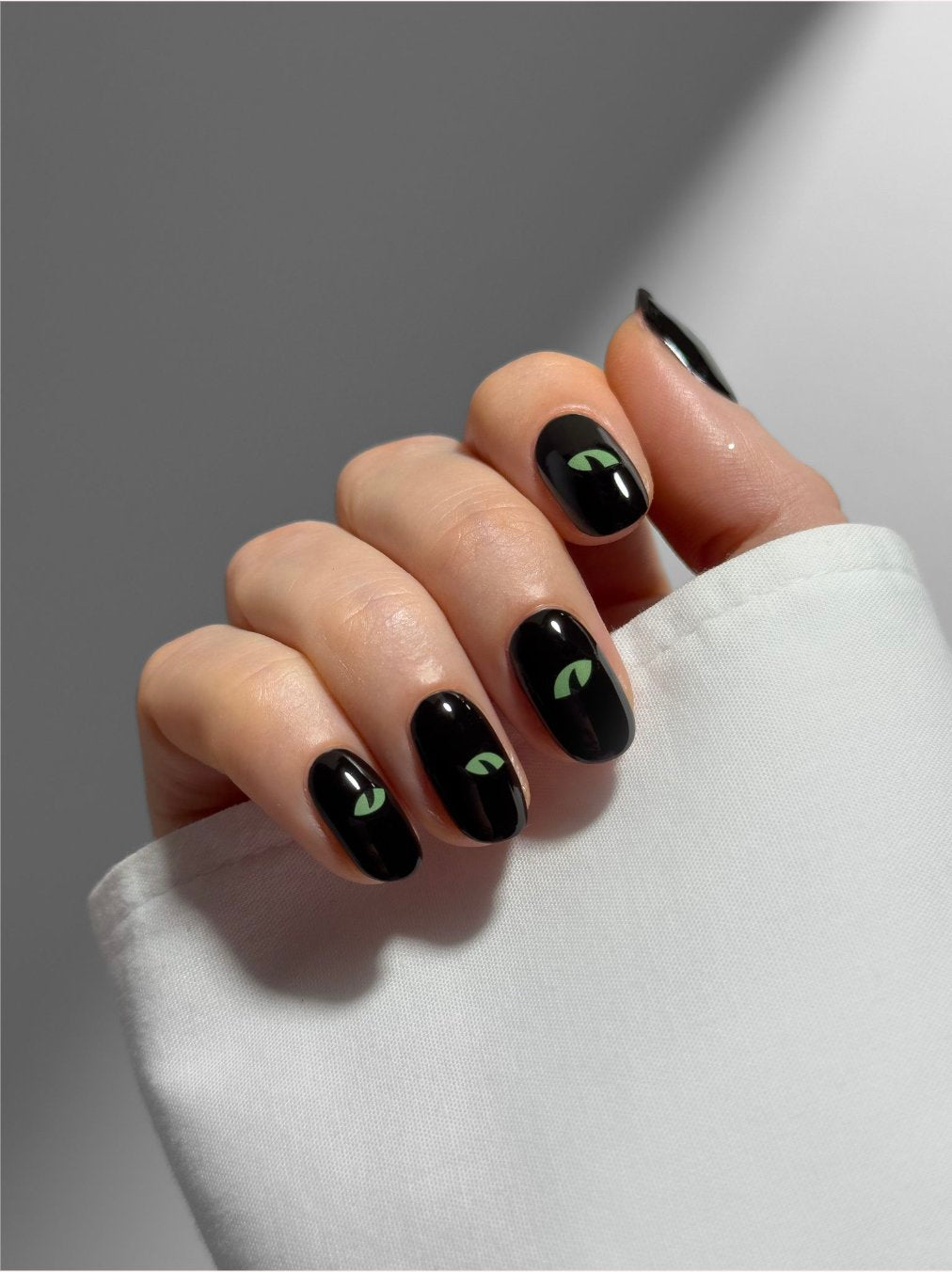 A hand with black nail polish featuring yellow cat-eye designs on each fingernail, holding a white cloth.