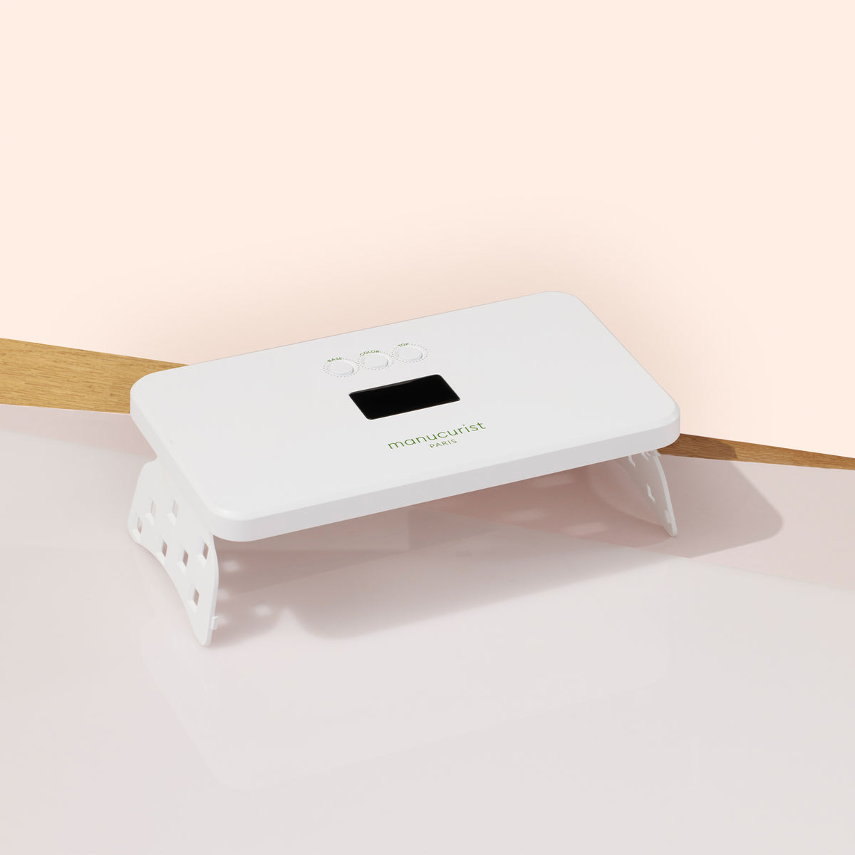 The Manucurist Green Flash™ Premium 36W Lamp—a white, rectangular LED lamp with a digital display and button controls—sits on a light pink and wood surface, ideal for quickly drying Green Flash gel polish.