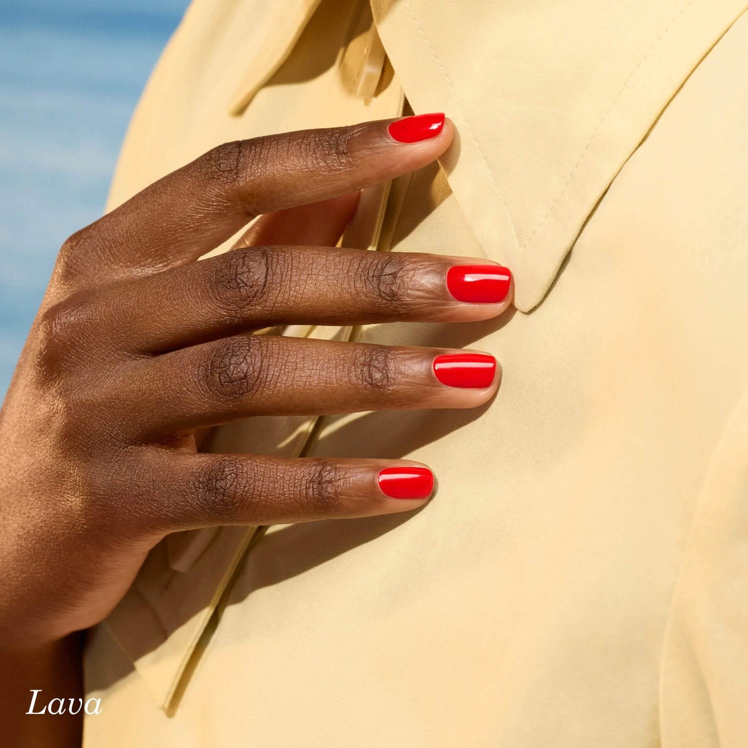 A close-up of a hand with bright red polished nails gently resting on a pale yellow collared shirt. The background is softly blurred, and the word Lava appears in the lower left corner.