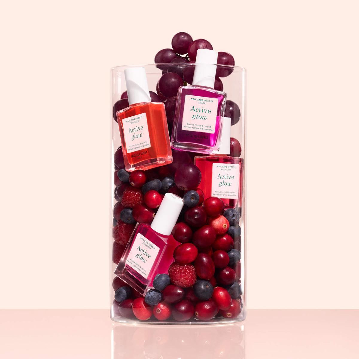 Un pack personnalisable de 5 Active™ Manucurist est présenté dans un contenant en verre transparent avec des raisins rouges, des canneberges, des myrtilles et des framboises, créant une composition unique sur un fond rose clair.