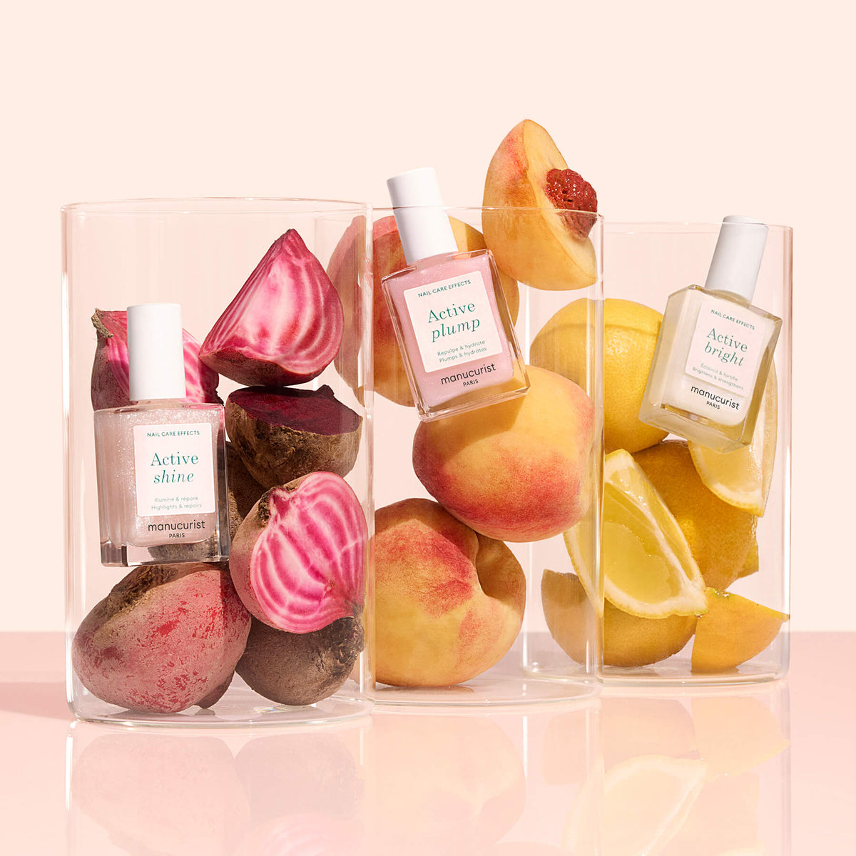 Trois contenants en verre transparent renferment chacun un vernis à ongles Manucurist Customizable Active en pack de 5 et des produits frais : des betteraves avec Active Shine, des pêches avec Active Plump et des citrons avec Active Bright, sur un fond clair.