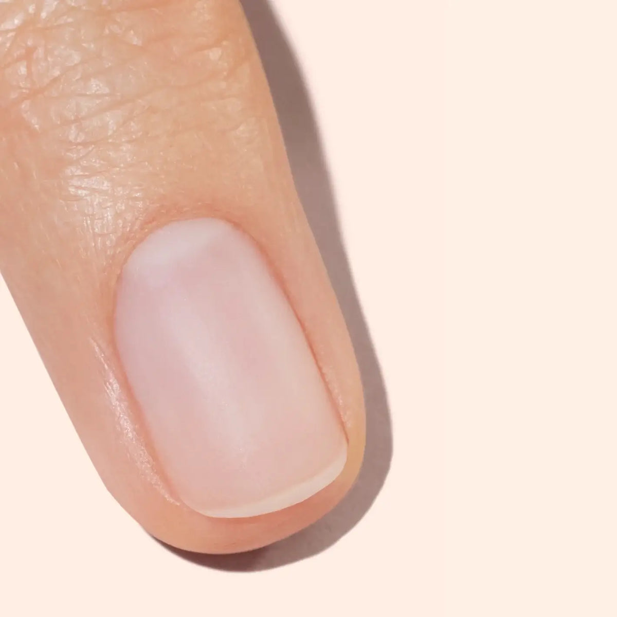 A close-up of a persons clean, neatly trimmed fingernail and fingertip on a light beige background.