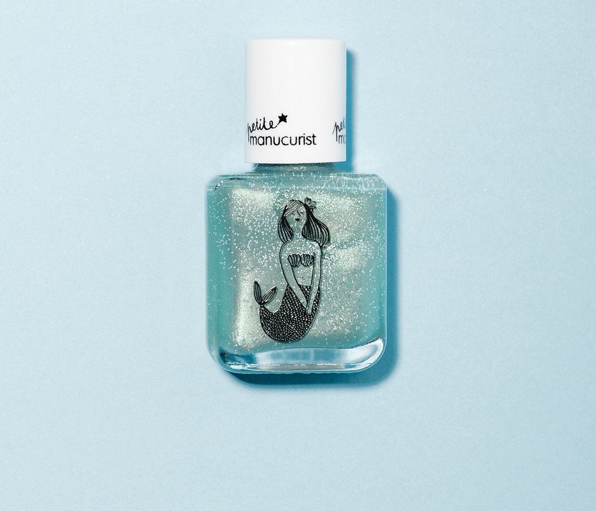 A clear nail polish bottle with a white cap, featuring an illustration of a glittery mermaid on the front, set against a light blue background.