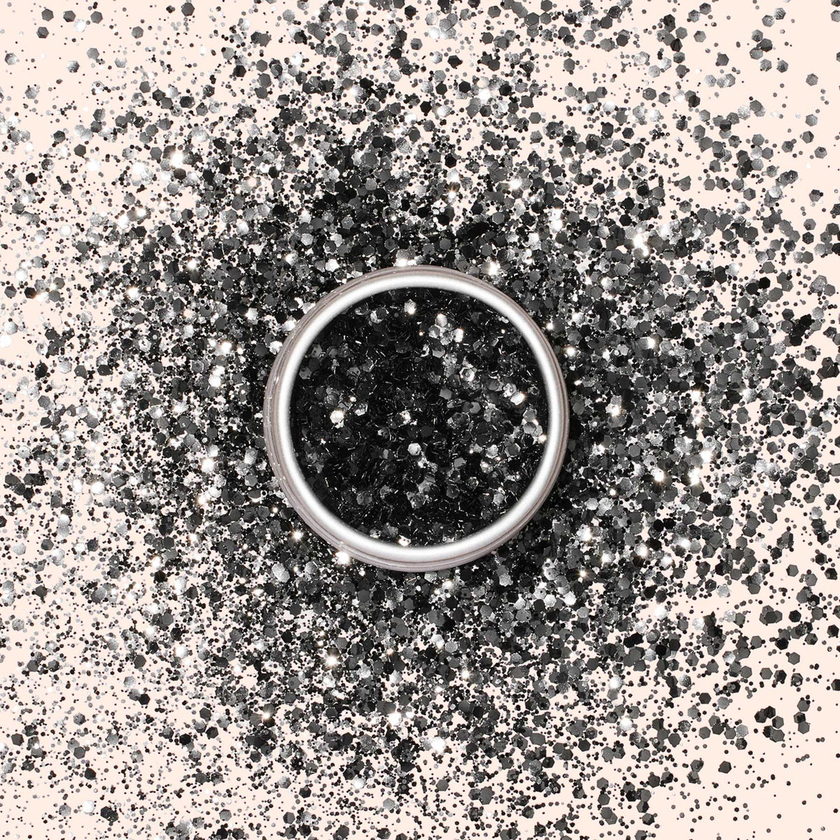 Une bague en argent repose sur une surface claire, entourée de Paillettes Biodégradables Manucurist noires et argentées, formant un motif circulaire scintillant autour de la bague.