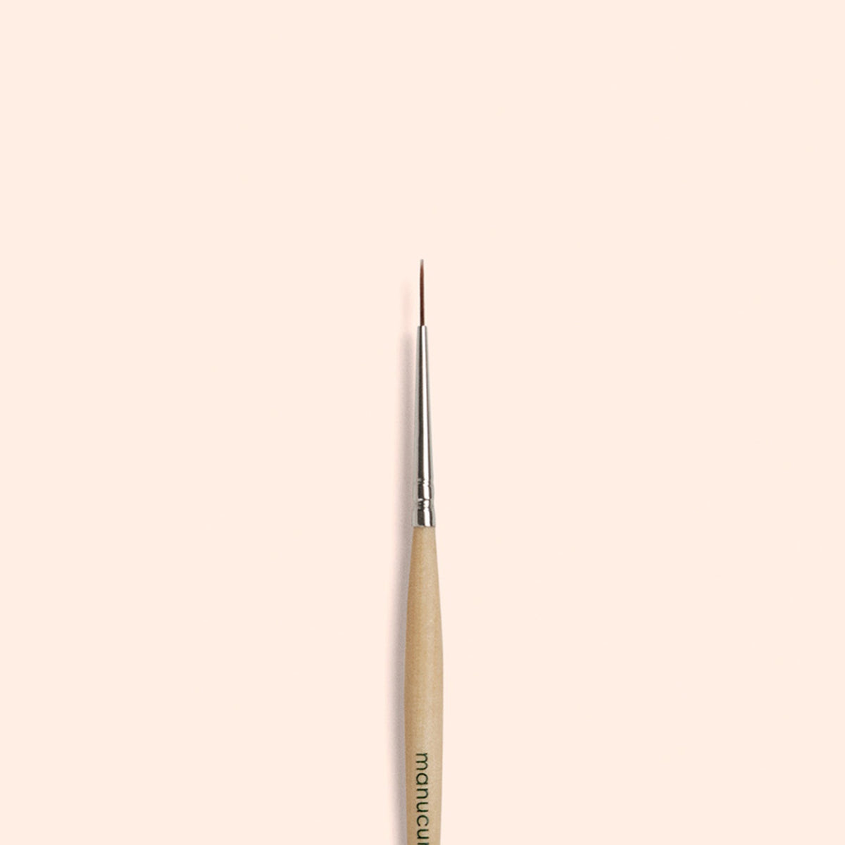 Le Liner Brush Manucurist, doté de poils synthétiques véganes et d’une pointe fine, est centré verticalement sur un fond beige clair uni.