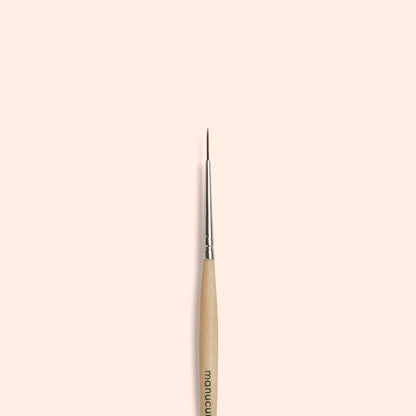 The Manucurist Liner Brush, featuring vegan synthetic bristles and a fine tip, is vertically centered on a simple light beige background.