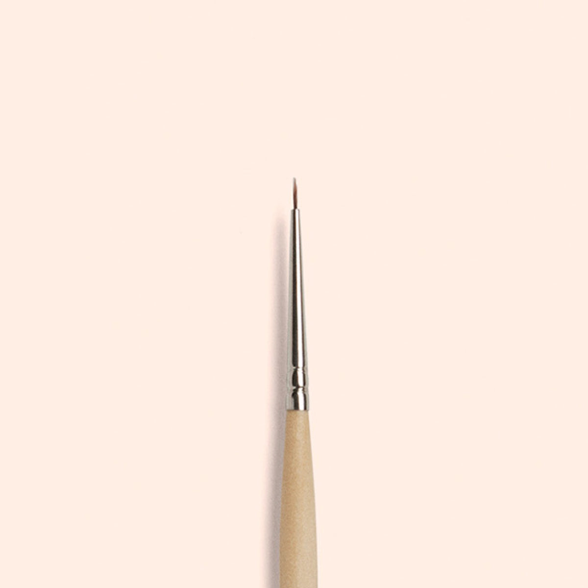 Le Fine Tip Brush Manucurist, composé de poils synthétiques vegan, d’un manche en bois et d’une virole argentée, se tient verticalement sur un fond beige clair — parfait pour créer un nail art précis.