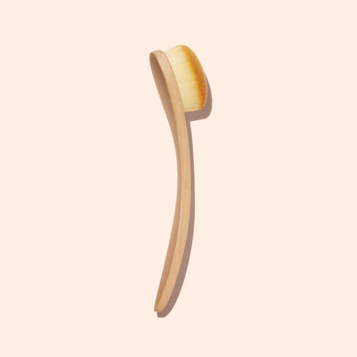 Le Dust Brush de Manucurist présente un corps en bois, un long manche incurvé et des poils véganes doux, sur un fond beige clair.