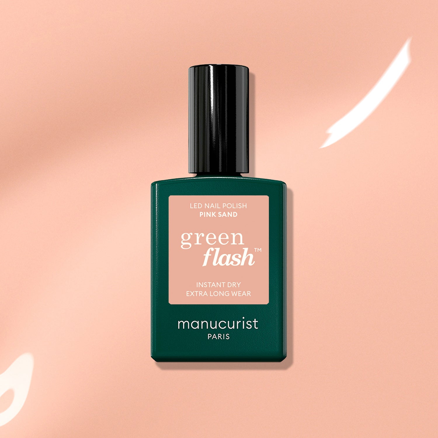 A bottle of Manucurist Pink Sand gel polish with subtle orange undertones rests on a softly lit peach background with white highlights.