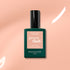 A bottle of Manucurist Pink Sand gel polish with subtle orange undertones rests on a softly lit peach background with white highlights.