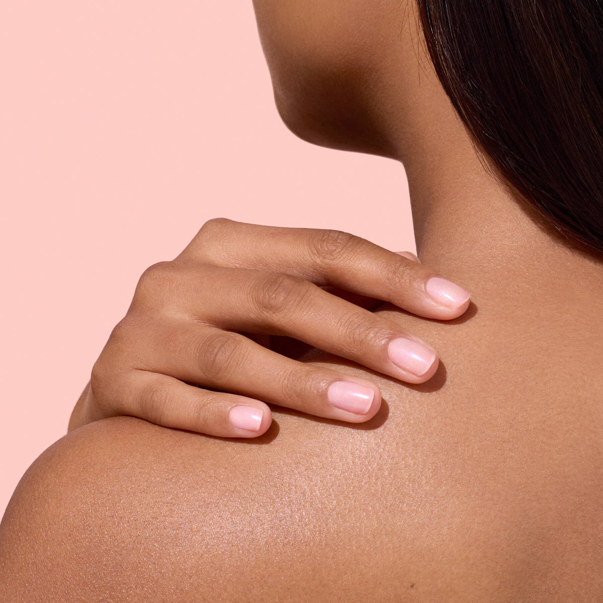 Une personne à la peau lisse touche son épaule nue avec des ongles impeccablement manucurés vernis avec l&