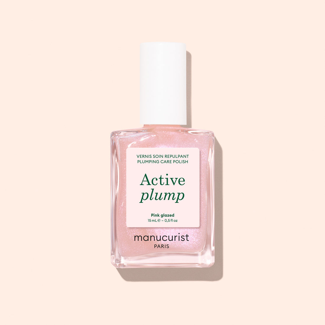 A bottle of Manucurist Active Plump Pink Glazed nail polish with a white cap and light pink liquid, set against a light beige background. The label mentions "Plumps hydrates for beautifully hydrated nails" and "Paris.