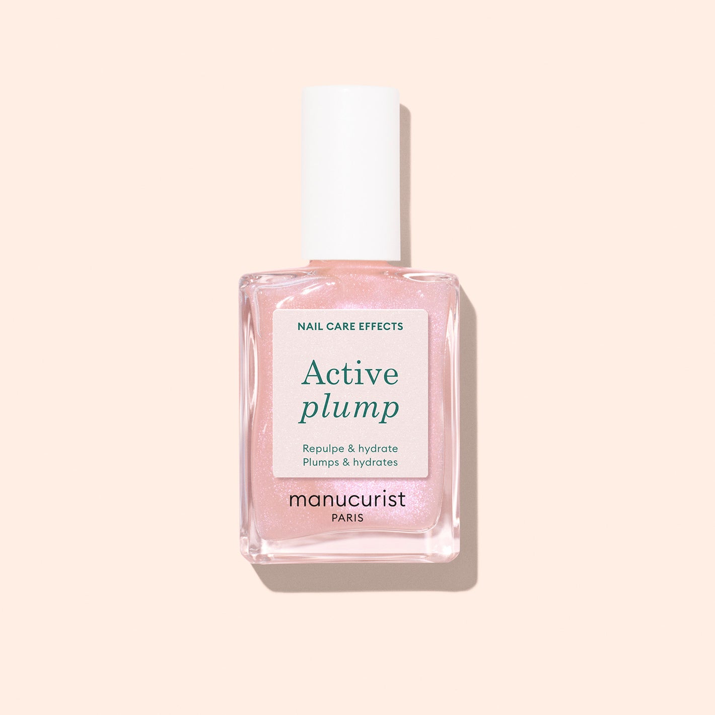 Active Plump nail polish by manucurist Paris features a light pink shade, white cap, and label highlighting its plumping and hydrating effects, shown on a pale peach background for visibly hydrated nails.
