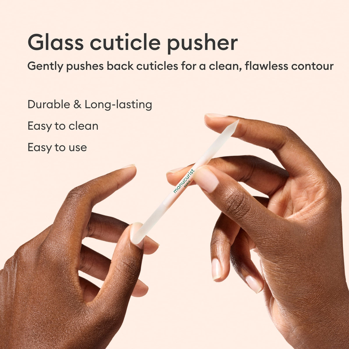 Deux mains tiennent le Repousse-cuticules en verre Manucurist sur fond beige. Cet outil professionnel redessine délicatement le contour des ongles, est résistant, durable, facile à nettoyer et simple à utiliser.