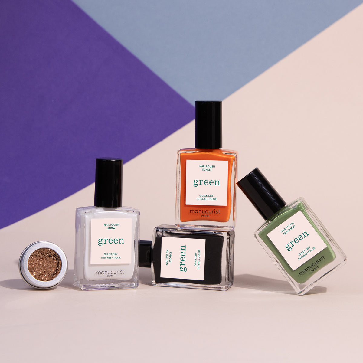 Quatre flacons de vernis à ongles Pumpkin Patch de Manucurist, transparents, orange, noirs et verts, sont présentés avec un petit pot ouvert de paillettes dorées sur un fond géométrique violet et beige — idéal pour le Nail Art d’Halloween.