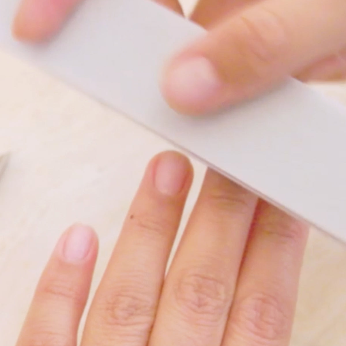 A close-up of a person filing their fingernails with a white nail file, focusing on their hands and fingers.