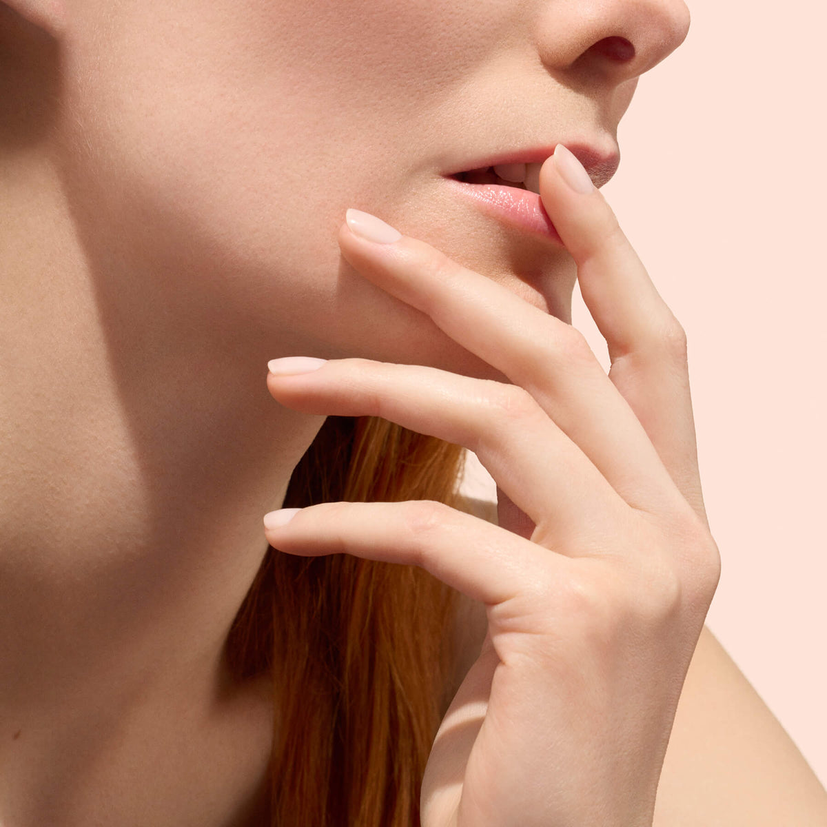 Gros plan sur une femme touchant ses lèvres avec ses doigts, mettant en valeur une peau lisse et des ongles au rendu naturel sublimés par Manucurist Active™ Smooth 00, sur un fond rose poudré.