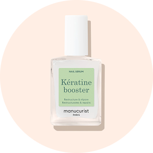 Un flacon en verre de sérum pour les ongles Manucurist Paris, étiqueté Kératine booster, avec une étiquette verte, un bouchon blanc et un fond circulaire pêche doux.