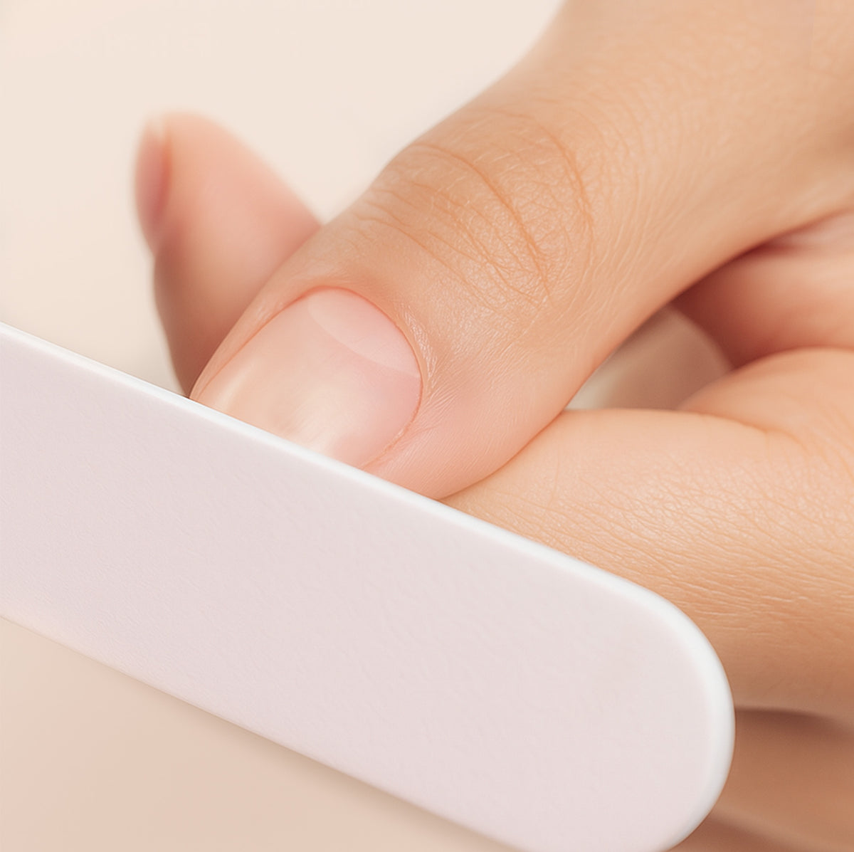 A close-up of a hand filing a fingernail with a white nail file against a soft, neutral background. The nail and fingers appear clean and well-groomed.