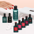 A hand with red polished nails reaches toward the Manucurist-test Green Flash™ Welcome Kit, featuring gel polish, acetone-free remover, clips, and a UV nail lamp on a light pink surface.