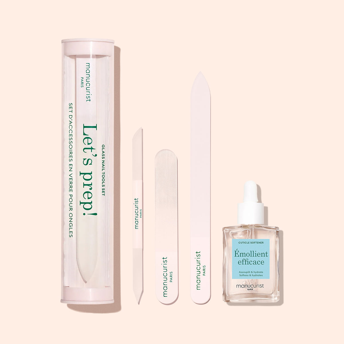 Le repousse-cuticules en verre Manucurist est présenté avec un tube « Let’s prep! », trois limes à ongles assorties et une huile de manucure avec compte-gouttes, le tout soigneusement disposé sur un fond rose pâle.