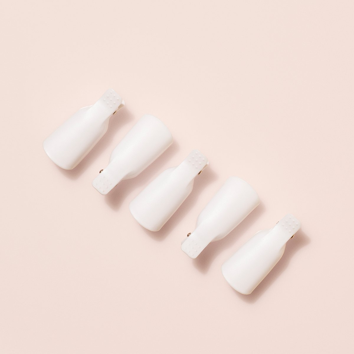 Five Manucurist-us Green Flash™ Remover Clips, perfect for gentle nail polish and gel polish removal, are arranged diagonally on a light beige background, evenly spaced with their open ends facing downward.
