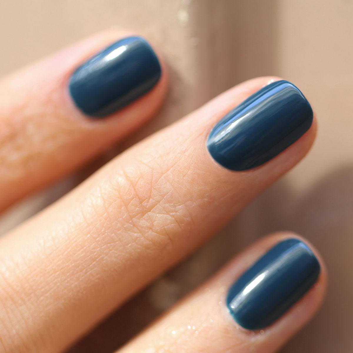 Gros plan d’une main aux ongles soigneusement manucurés, vernis avec le vernis gel Dark Clover de Manucurist, les doigts posés sur une surface beige lisse.