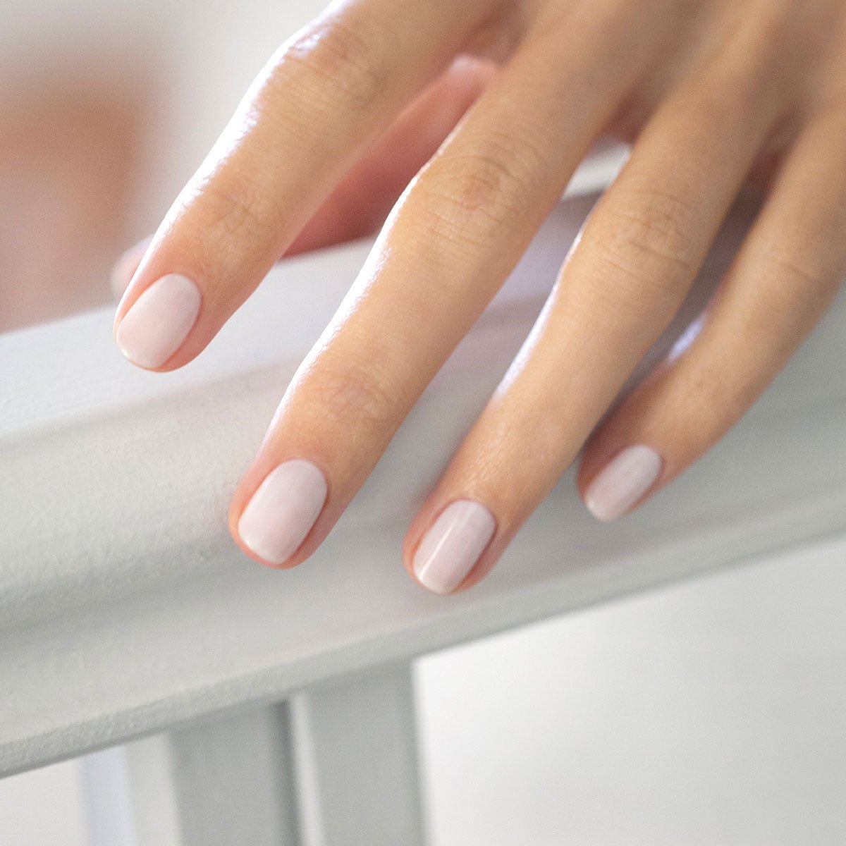 Gros plan sur une main aux ongles soigneusement manucurés, vernis avec Milky White de Manucurist, un vernis gel doux et transparent, reposant délicatement sur une surface blanche.