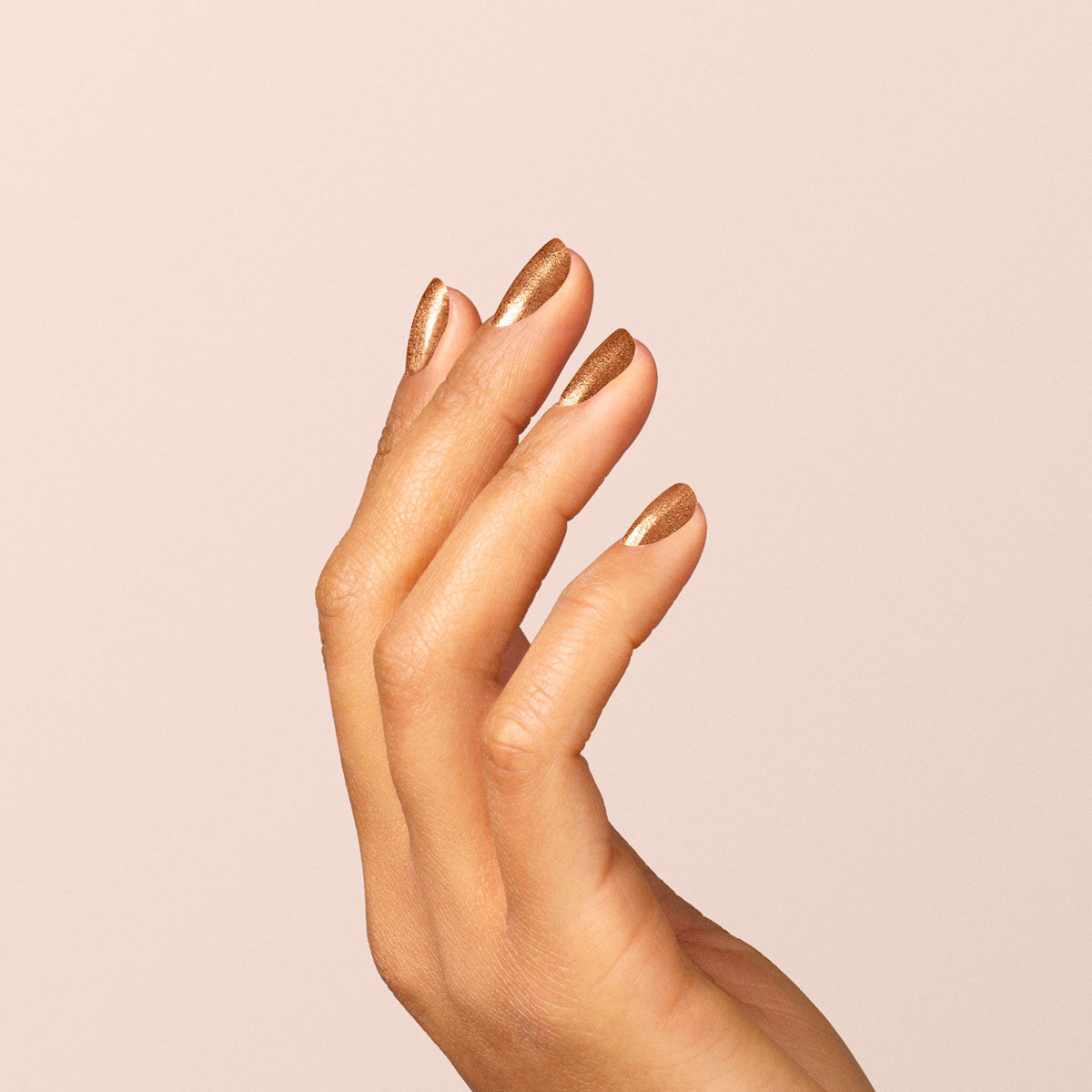 Une main aux ongles soigneusement manucurés, vernis avec le gel semi-permanent cuivré irisé Bronzé de Manucurist, est présentée sur un fond beige clair uni, les doigts légèrement courbés et détendus.
