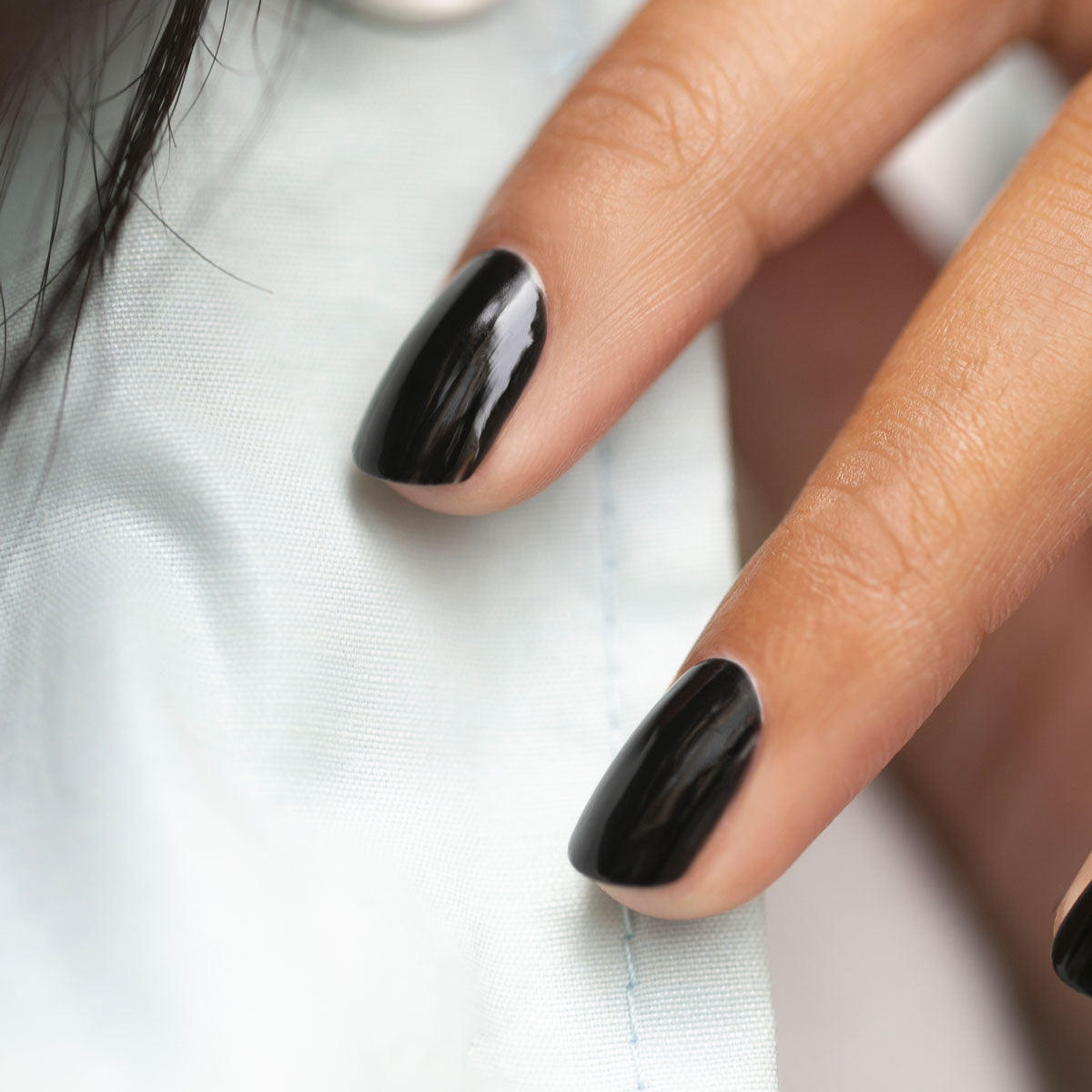 Gros plan sur une main aux ongles soigneusement manucurés, peints avec le vernis noir Licorice de Manucurist, reposant sur un tissu bleu clair.