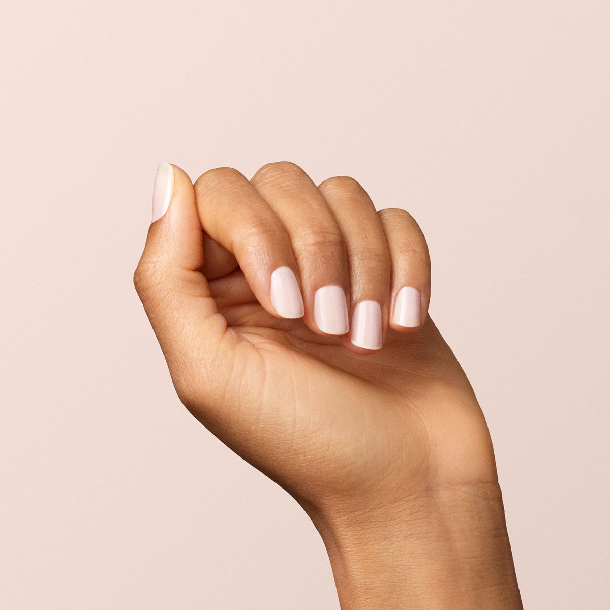 A hand with neatly manicured nails painted in Milky White by Manucurist is held against a plain, light beige background.