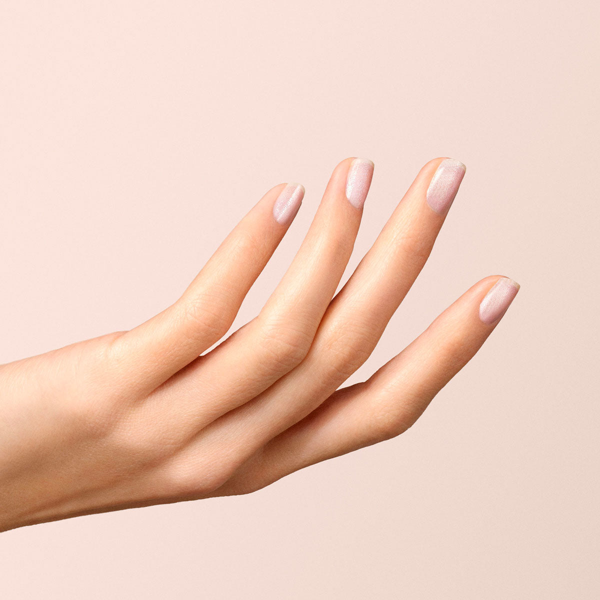 A hand with light skin tone and neatly manicured nails painted in Manucurist’s Diamant, a soft silver shade, is shown against a beige background with fingers slightly spread.