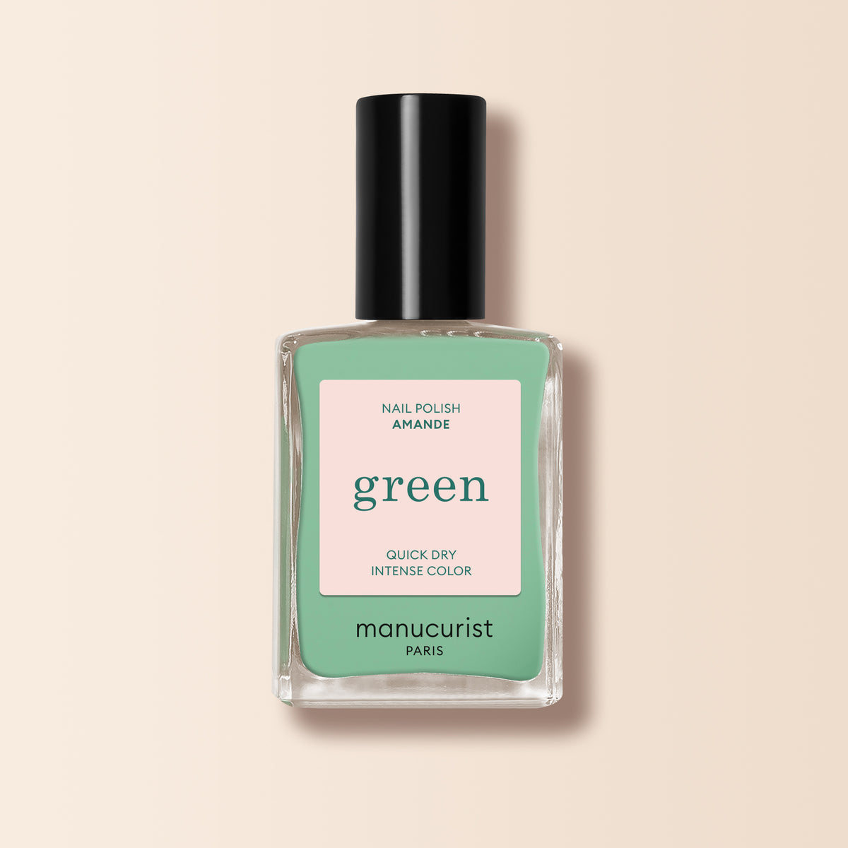 Un flacon de vernis à ongles Manucurist Amande de la gamme Green™, avec une teinte vert menthe et un capuchon noir, portant la mention "Quick Dry Intense Color," est présenté sur un fond beige clair.