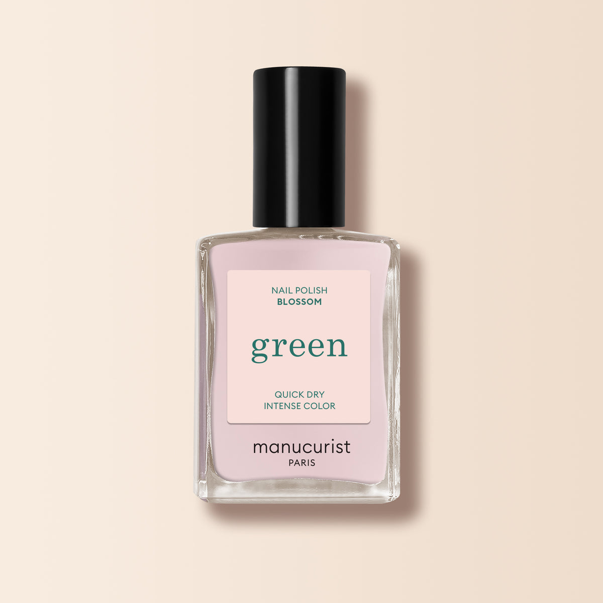 A bottle of Manucurist nail polish in the shade “Blossom,” featuring a creamy light pink color, black cap, and square transparent glass bottle from the Green range is displayed against a beige background.