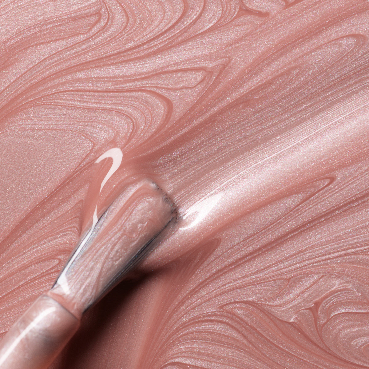Gros plan d’un pinceau appliquant Carnation de Manucurist — un vernis gel rose doré scintillant — sur une surface rose nacré marbrée, créant des stries lisses et brillantes avec la formule Green Flash™.
