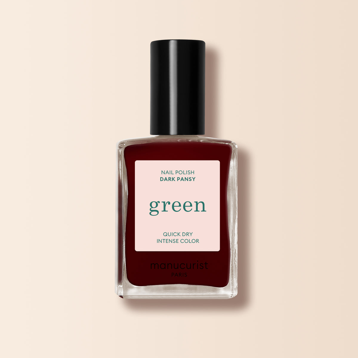 Un flacon de vernis à ongles Manucurist dans la teinte Dark Pansy, avec un rouge velours profond, un capuchon noir et une étiquette de la gamme Green™ sur fond beige.