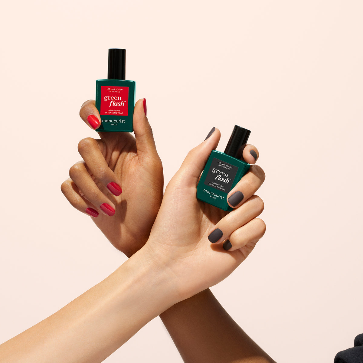Deux mains aux ongles manucurés tiennent des flacons verts de Matte Top Coat de Manucurist ; l’une a les ongles rouges, l’autre gris foncé, toutes deux mettant en avant une formule d’origine végétale sur un fond clair uni.