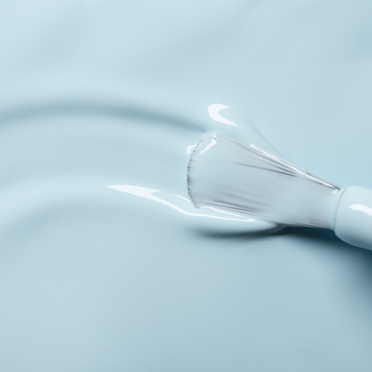 Gros plan sur un pinceau de vernis à ongles Manucurist Light Blue appliquant une couleur bleu pastel brillante sur une surface lisse, créant une couche brillante et uniforme.
