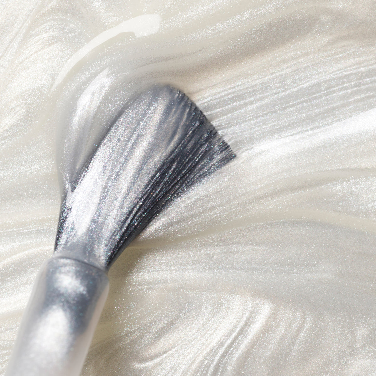 Gros plan sur un pinceau étalant le vernis Moon de Manucurist, un vernis semi-permanent blanc nacré scintillant, sur une surface lisse pour créer de doux reflets métallisés.