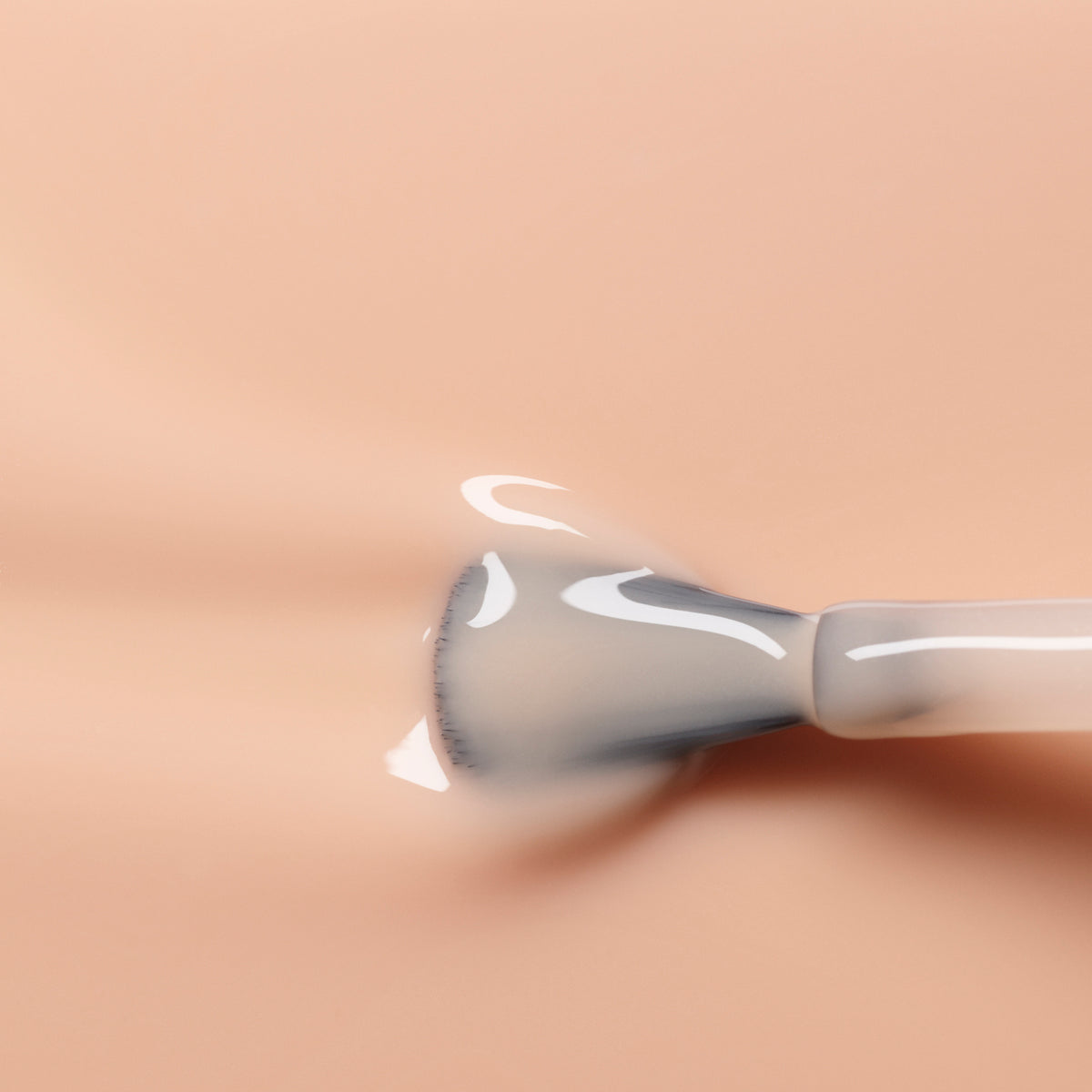 A close-up of a Manucurist Beige nail polish brush applying a glossy, sheer nude gel coat onto a smooth surface.