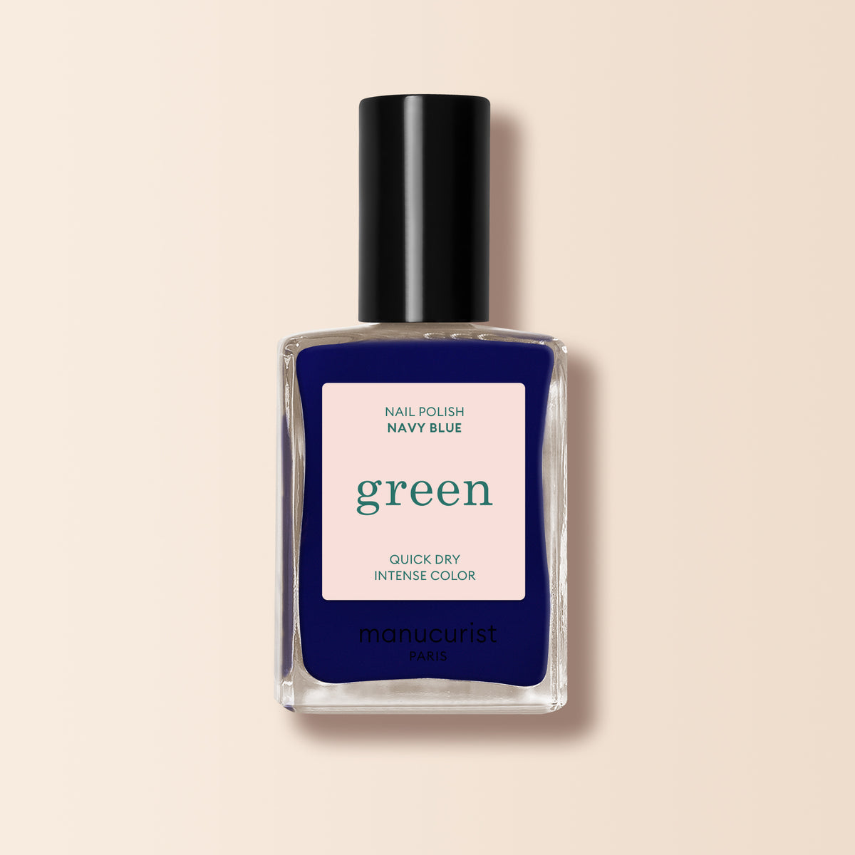A bottle of Manucurist Navy Blue nail polish from the Green range with a black cap. The label says Nail Polish Navy Blue, Quick Dry Intense Color, and manucurist Paris. The background is soft beige.