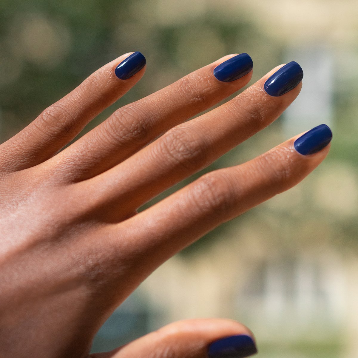 A hand with medium brown skin displays neatly manicured nails painted in Manucurist&