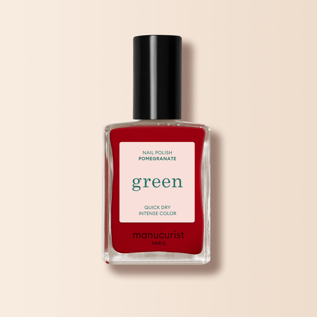 A bottle of Manucurist Pomegranate nail polish, featuring a red shade with a black cap and white label displaying green and red text, is shown against a light beige background.