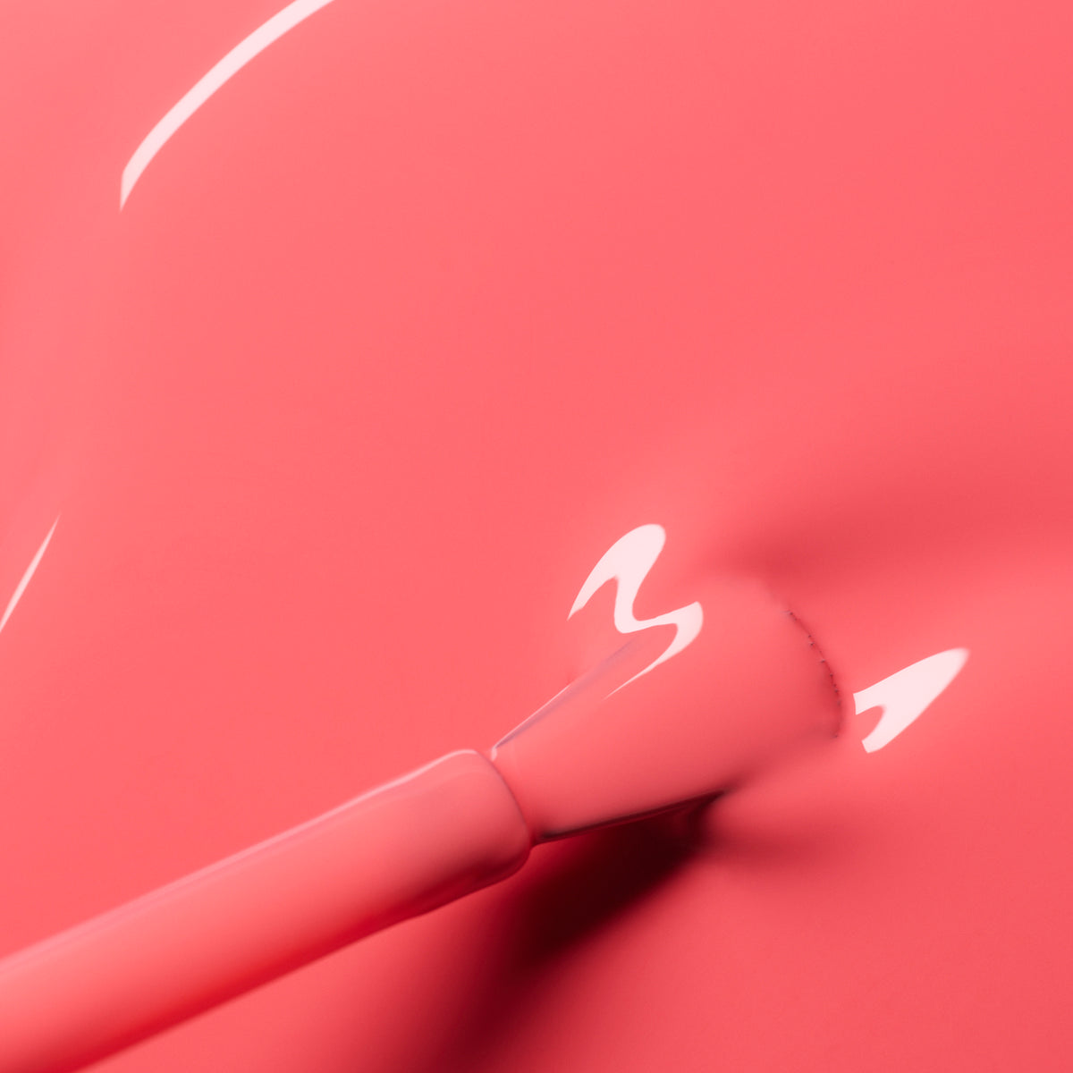 Close-up of a brush applying Manucurist Capucine, a glossy coral pink nail polish with a smooth, shiny finish and visible reflections.