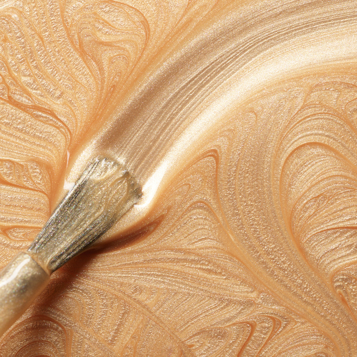 A close-up of a brush spreading shimmering, metallic gold paint with swirling patterns—evoking the brilliance of Manucurist&