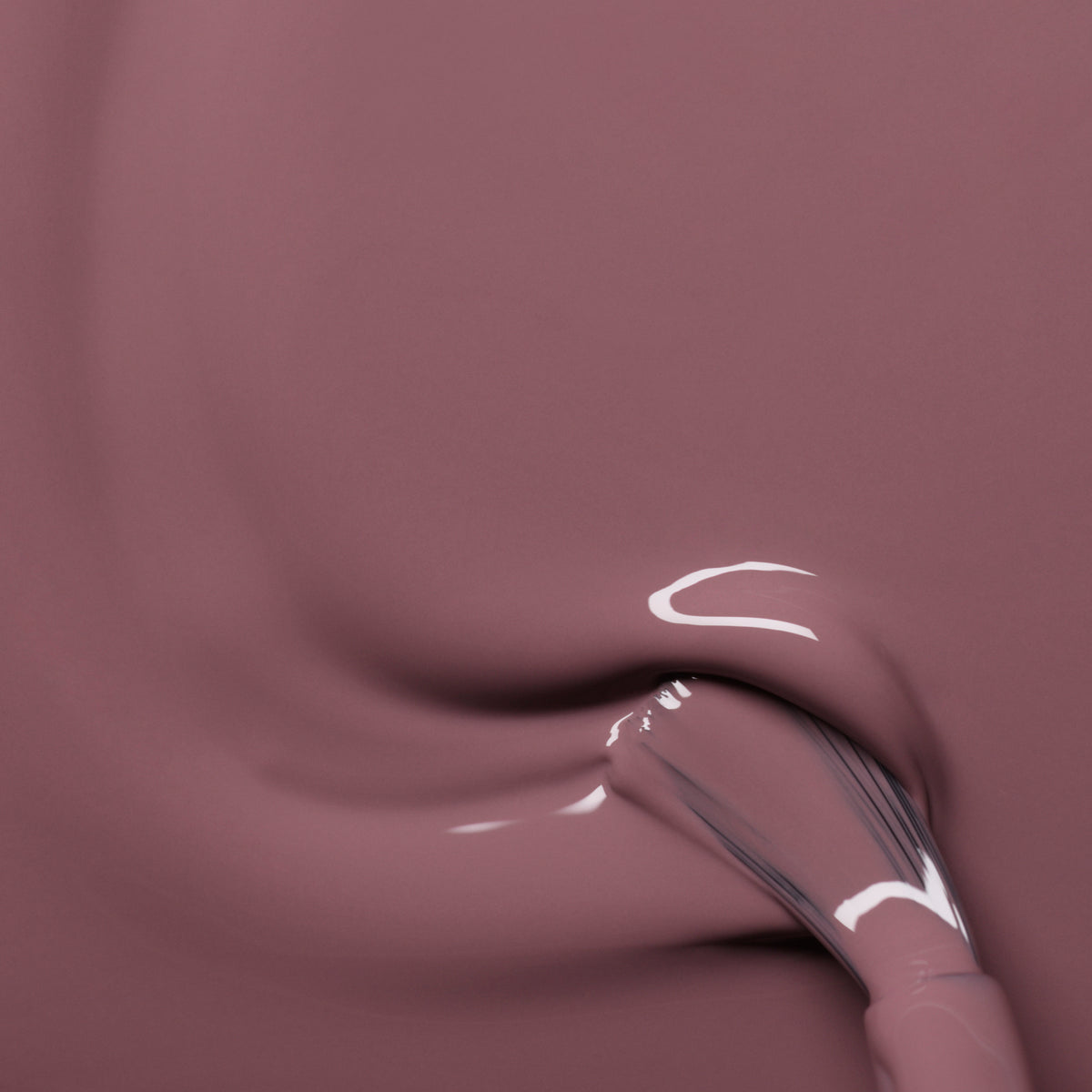 Gros plan sur un pinceau appliquant le vernis lisse Rose Mountbatten de Manucurist, créant des traces fluides et brillantes de rose camouflage.
