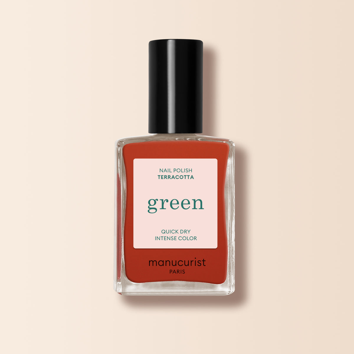 A bottle of Manucurist Terracotta nail polish in a scorched red earth shade, featuring a black cap and quick dry intense color label, displayed against a light beige background.