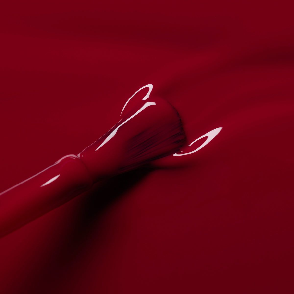A close-up of the Manucurist Violeta nail polish brush coating a surface with glossy burgundy purple polish. The bristles and handle are partly covered in the shiny polish, creating a sleek, vibrant look.