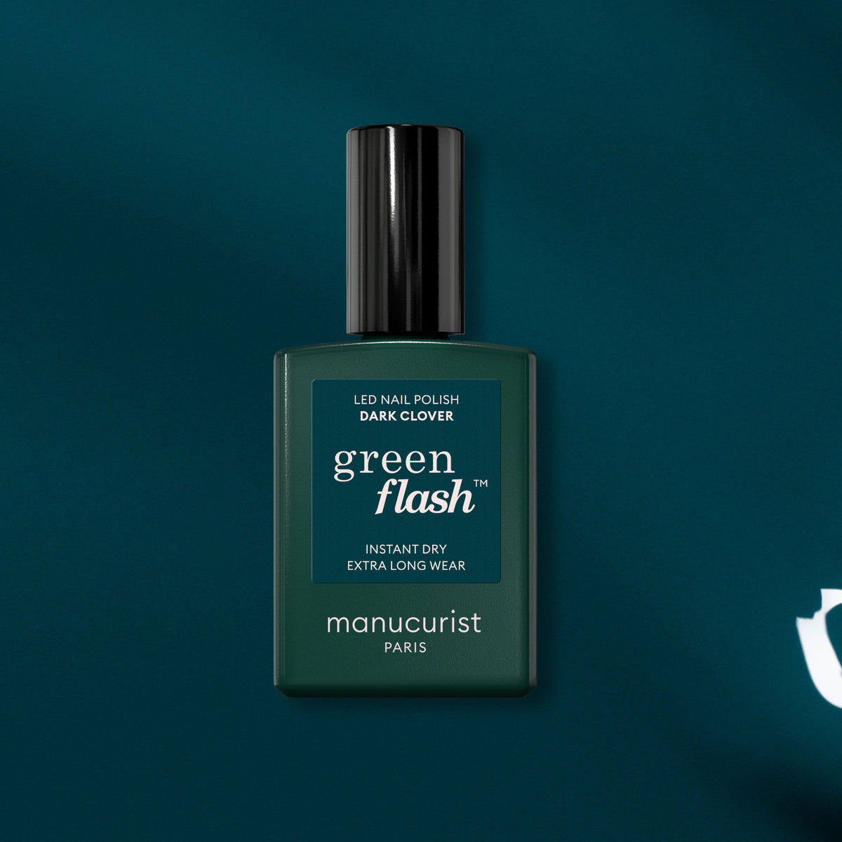 Un flacon de vernis gel Manucurist Dark Clover présenté sur un fond bleu canard foncé. Le flacon vert foncé, doté d&