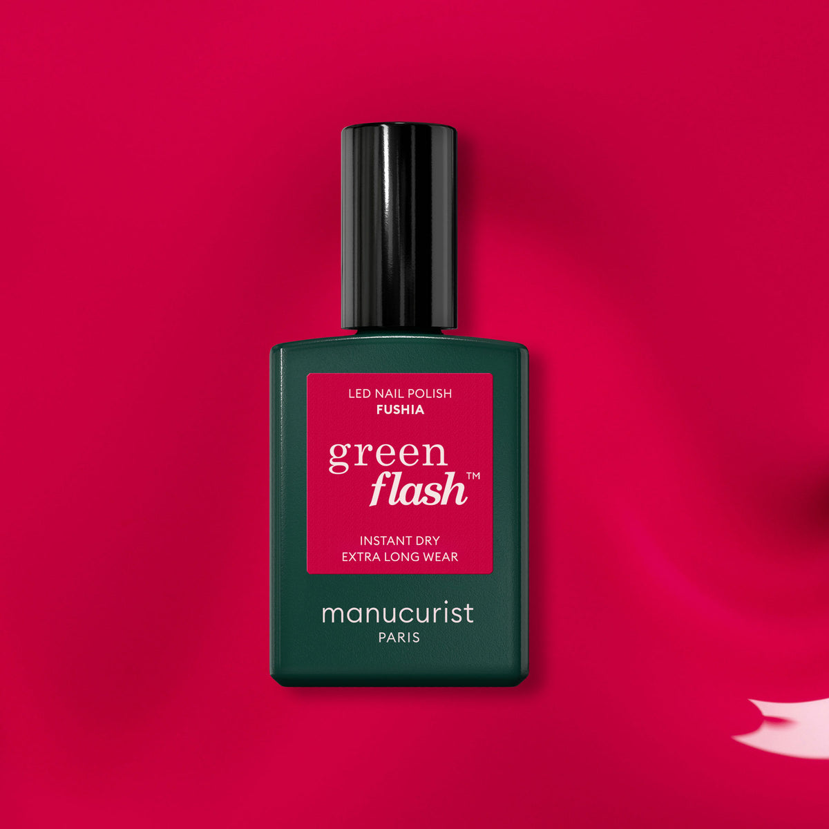 Un flacon de vernis Green Flash Manucurist teinte Fuchsia repose sur une surface rose éclatante, avec une touche de vernis fuchsia dans le coin inférieur droit.
